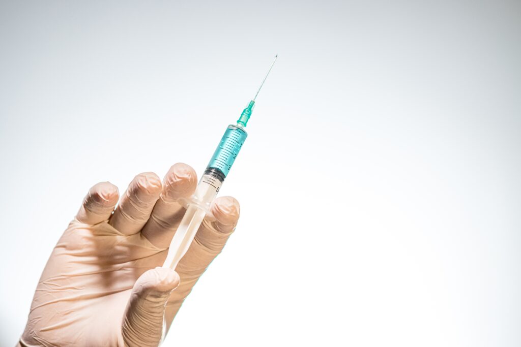 Closeup of a person with a latex glove holding a needle syringe isolated on a white background